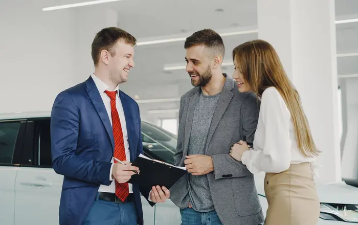 A car salesperson showing a new vehicle to a couple on a dealership showroom floor