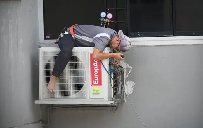 An HVAC technician servicing an outdoor air-conditioning condenser unit