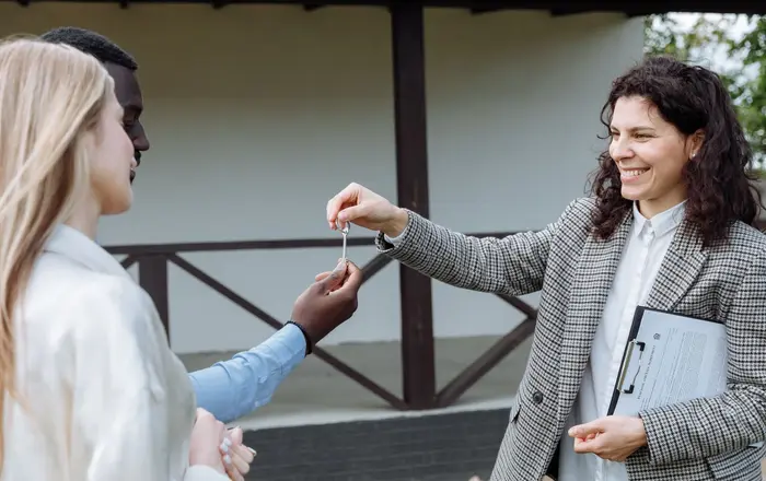 A real estate agent handing house keys to a happy buyer outside a new home