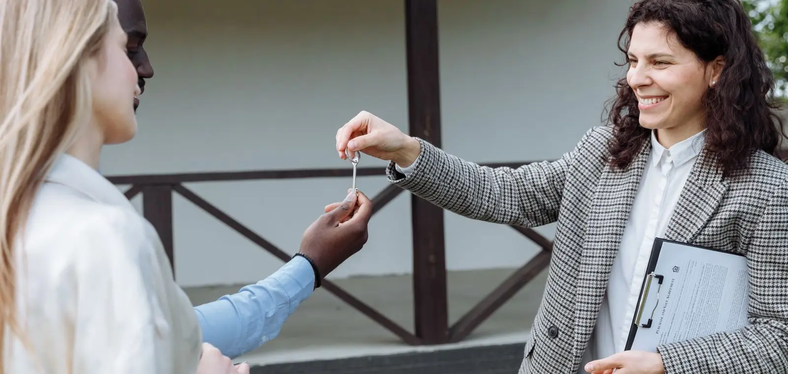 A real estate agent handing house keys to a happy buyer outside a new home