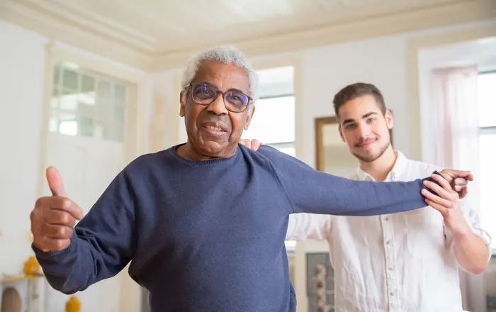 A caregiver supporting a smiling senior man at home